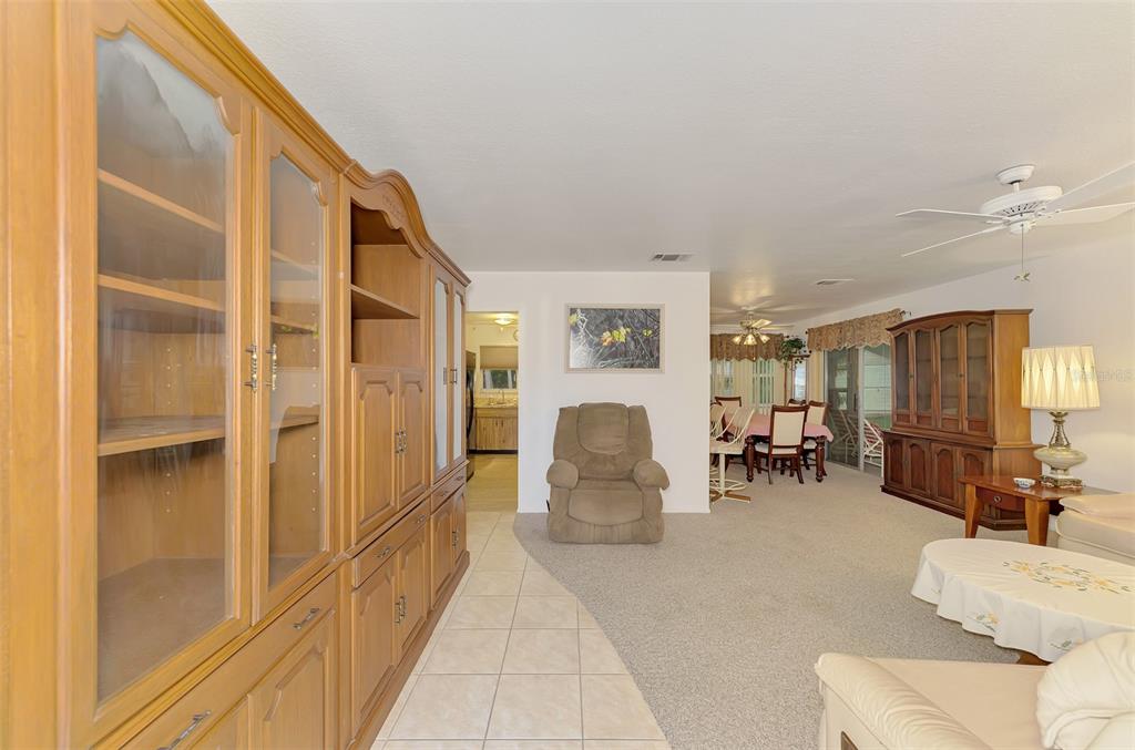 A living room with beige carpet, a large wooden wall unit, and a dining area — 5285 BROPHY STREET, NORTH PORT, FL