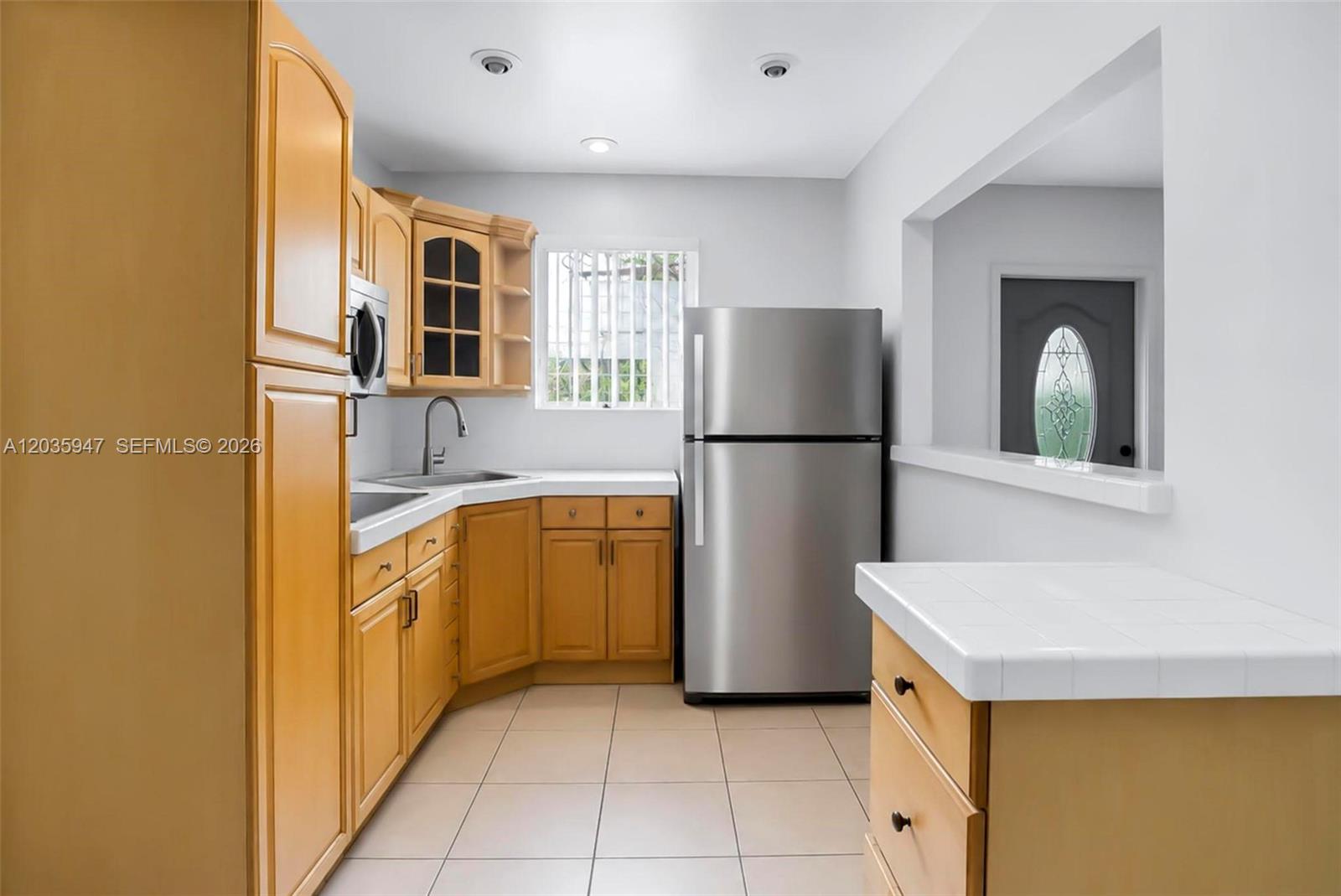 A kitchen features light wood cabinets, stainless steel appliances, and white tiled countertops — 2300 NW 9th St, Miami FL 33125, MIAMI, FL