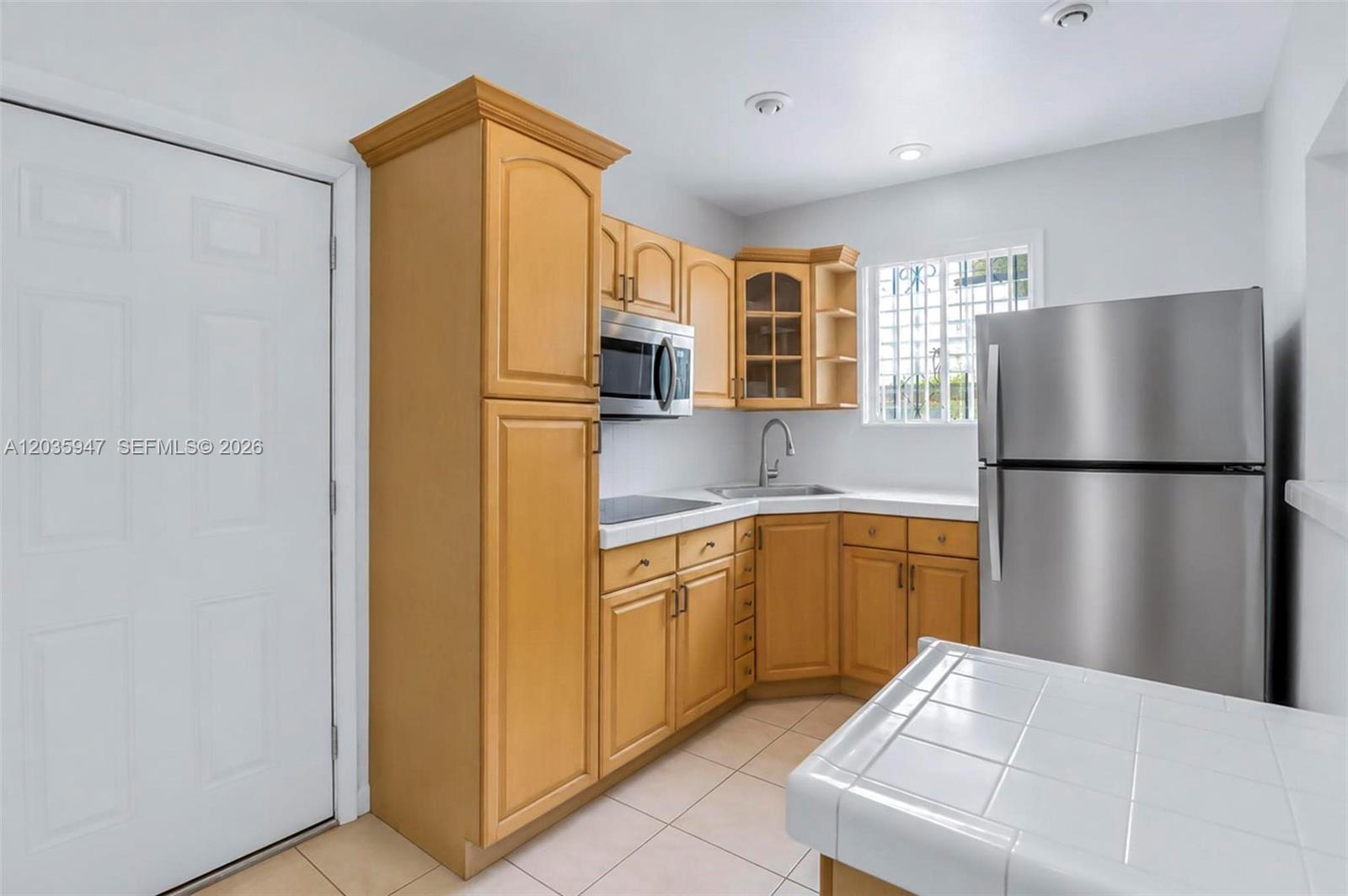 A kitchen features light wood cabinets, stainless steel appliances, and a white tiled countertop — 2300 NW 9th St, Miami FL 33125, MIAMI, FL