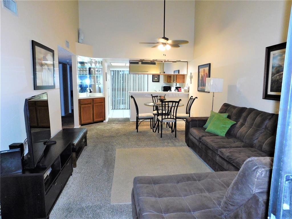 A living room with a vaulted ceiling, carpeted floors, a dining area, and a wet bar — 272 WOODLAKE WYNDE UNIT 272, OLDSMAR, FL