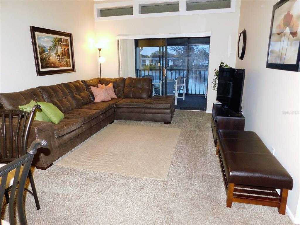 A living room features a brown sectional sofa, a television, and a sliding glass door — 272 WOODLAKE WYNDE UNIT 272, OLDSMAR, FL