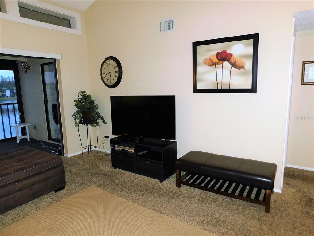 A living room features a television on a stand, a bench, wall art, and a balcony — 272 WOODLAKE WYNDE UNIT 272, OLDSMAR, FL