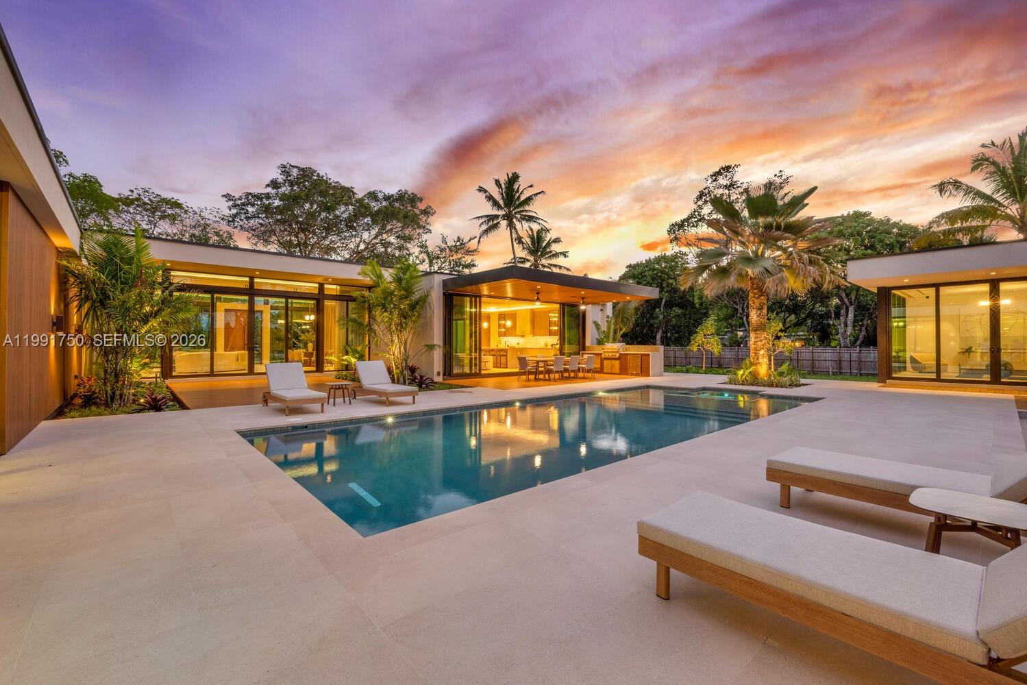 A modern house features a swimming pool, lounge chairs, and a patio at sunset — 7901 SW 120th St, Pinecrest FL 33156, PINECREST, FL