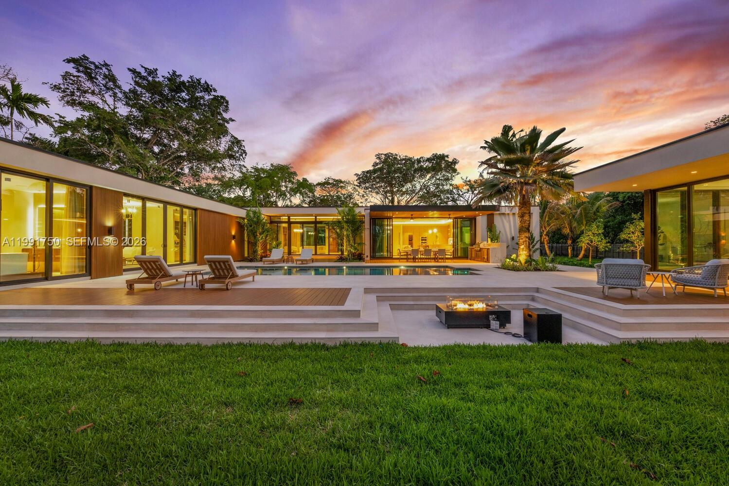 A modern home exterior features a swimming pool, sunken fire pit, and wood decking at sunset — 7901 SW 120th St, Pinecrest FL 33156, PINECREST, FL