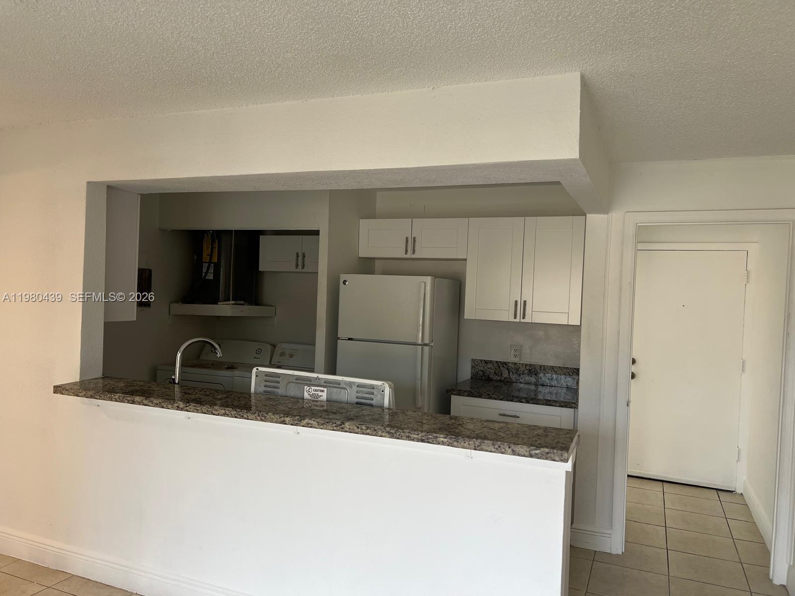A kitchen features white cabinets, granite countertops, a refrigerator, and a breakfast bar — 4435 Treehouse Ln # H, Tamarac FL 33319, TAMARAC, FL