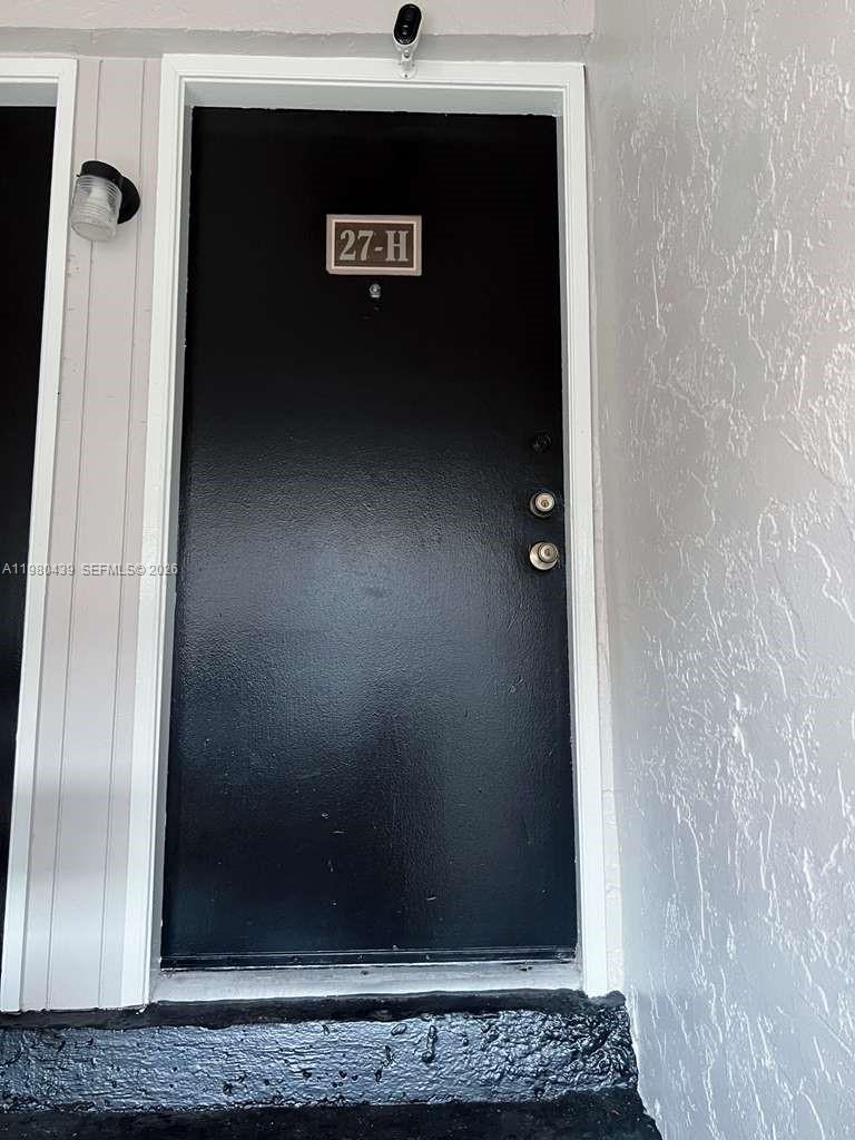 A black front door with the number 27-H is set in a white exterior wall — 4435 Treehouse Ln # H, Tamarac FL 33319, TAMARAC, FL
