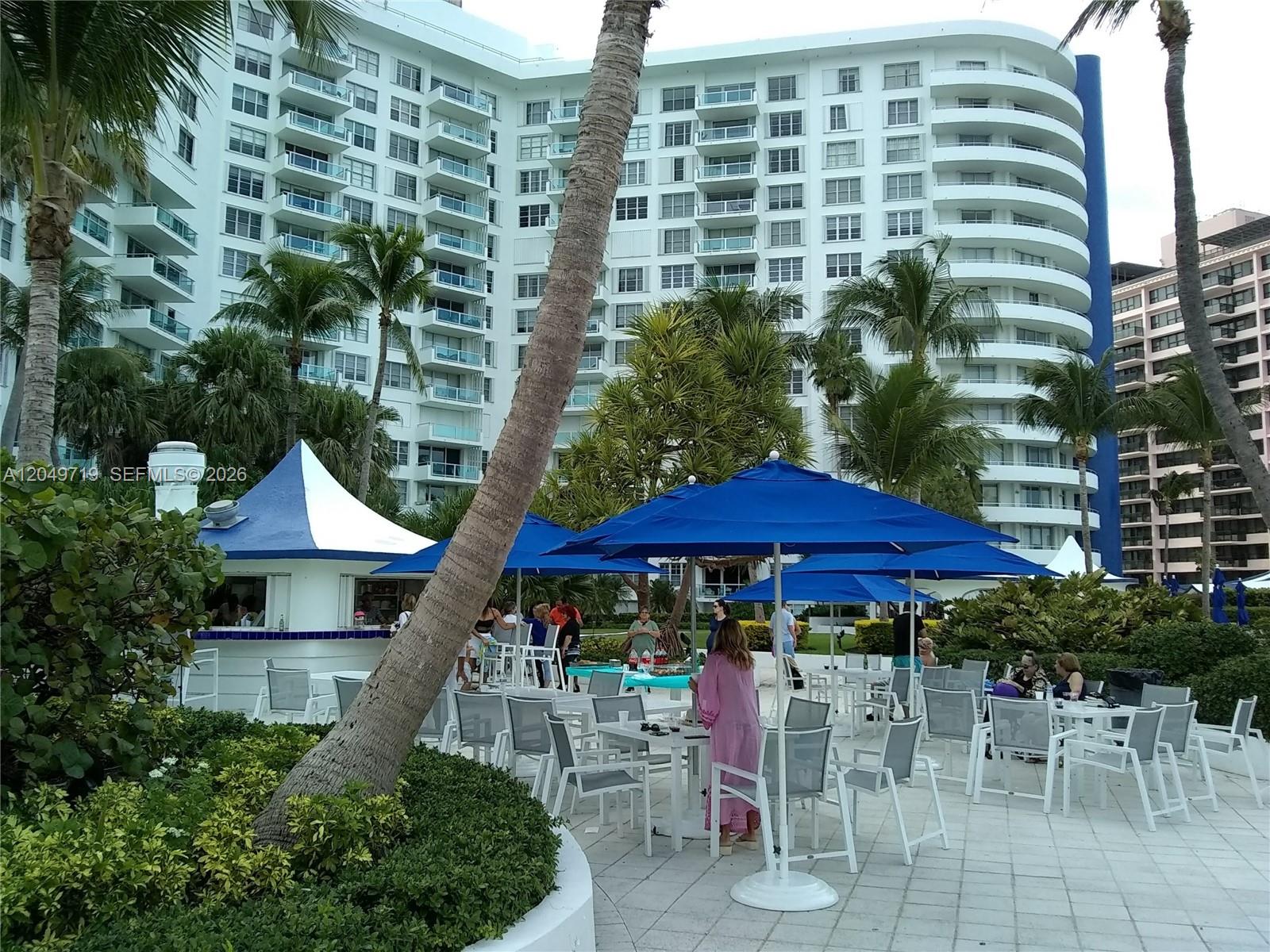 An outdoor patio area features tables with blue umbrellas in front of a large building — 5161 Collins Ave # 809, Miami Beach FL 33140, MIAMI BEACH, FL