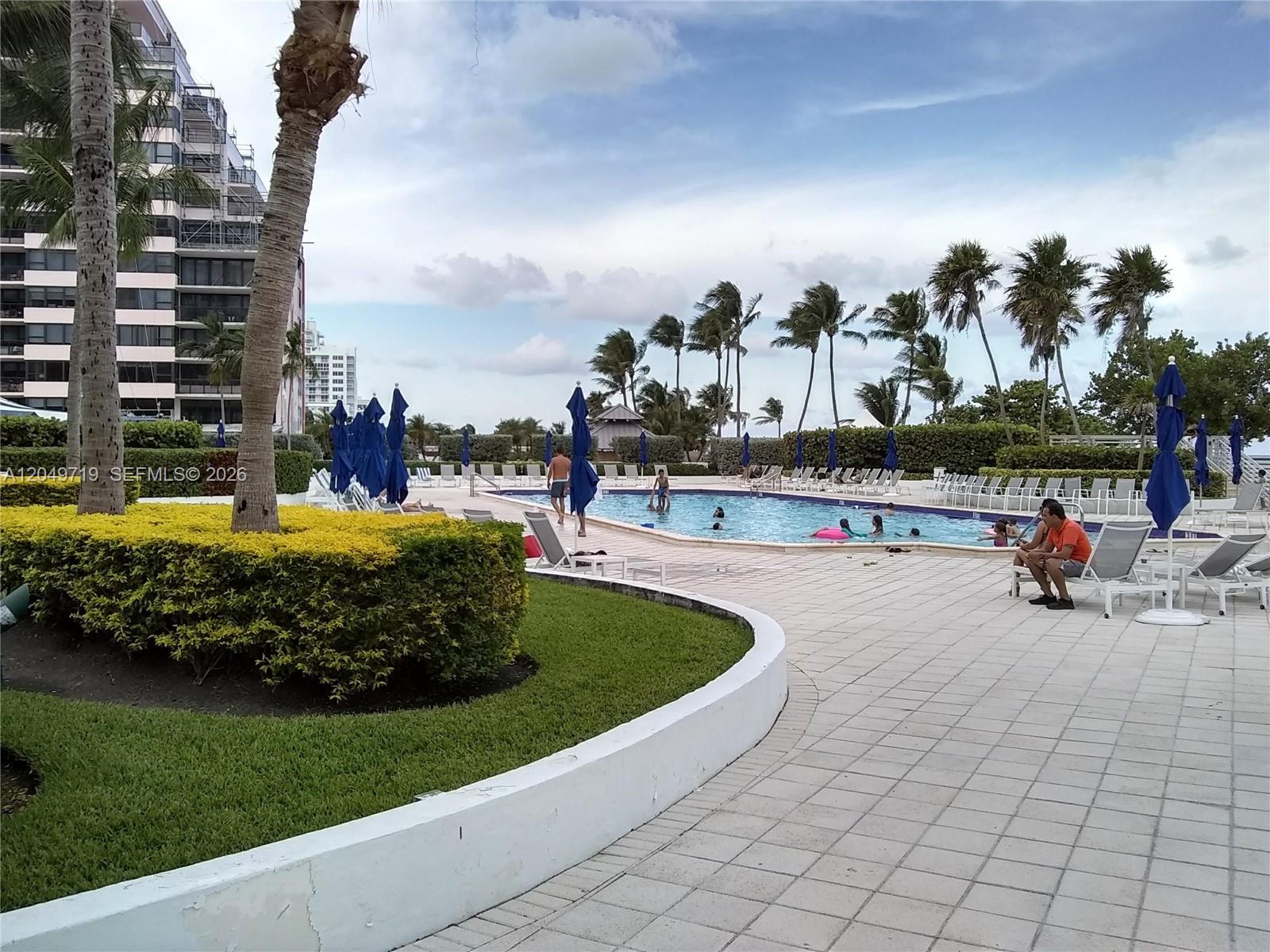An outdoor swimming pool area features lounge chairs, blue umbrellas, and palm trees — 5161 Collins Ave # 809, Miami Beach FL 33140, MIAMI BEACH, FL