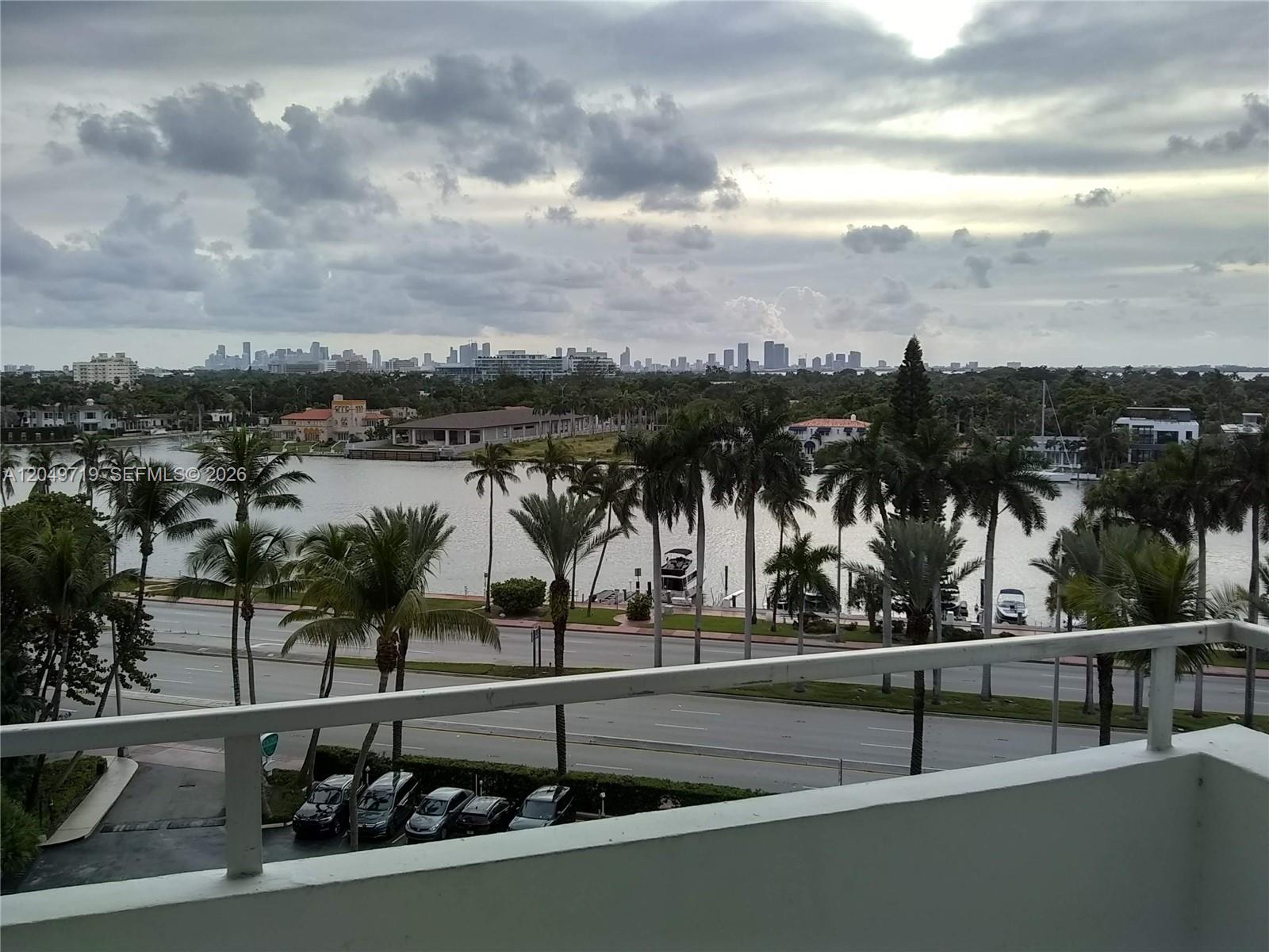 A balcony view overlooks a multi-lane road, palm trees, a waterway, and a distant city skyline — 5161 Collins Ave # 809, Miami Beach FL 33140, MIAMI BEACH, FL