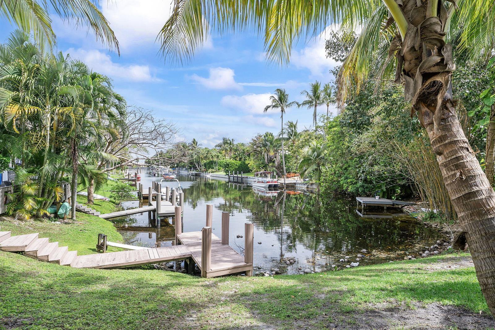 A wooden dock extends into a calm canal surrounded by lush tropical trees and vegetation — 981 Delray Lakes Drive, Delray Beach FL 33444, DELRAY BEACH, FL
