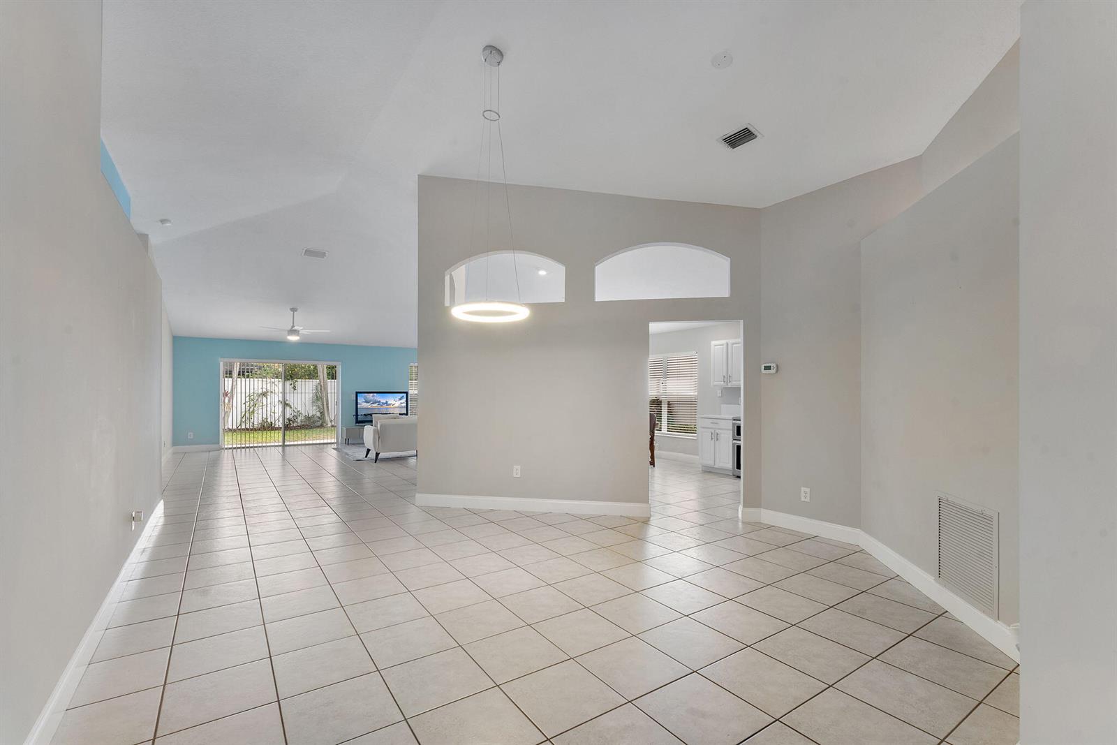 A spacious living area with light-colored tile floors, vaulted ceilings, and a modern pendant light — 981 Delray Lakes Drive, Delray Beach FL 33444, DELRAY BEACH, FL