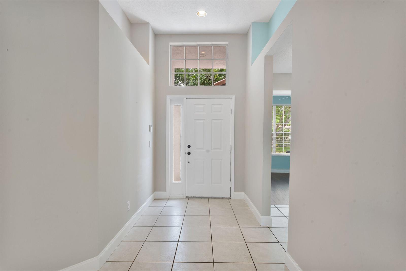 A bright entryway features light-colored tile flooring, a white front door, and a transom window — 981 Delray Lakes Drive, Delray Beach FL 33444, DELRAY BEACH, FL