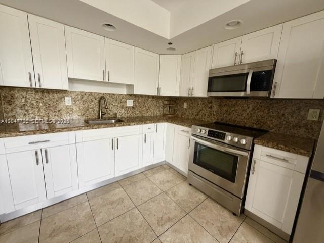 A kitchen features white cabinetry, granite countertops, stainless steel appliances, and tiled flooring — 8700 SW 133rd Ave Rd # 302, Miami FL 33183, MIAMI, FL