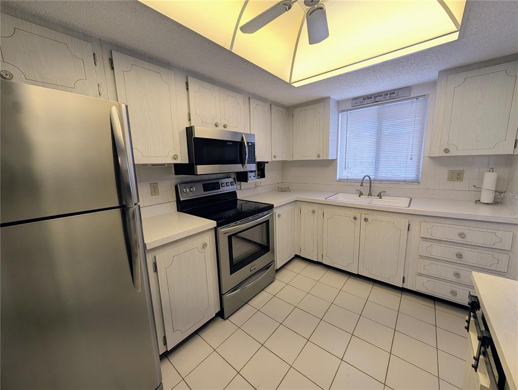 A kitchen features white cabinetry, stainless steel appliances, a white tile floor, and a window — 3564 LAKE BAYSHORE DRIVE UNIT K-203, BRADENTON, FL