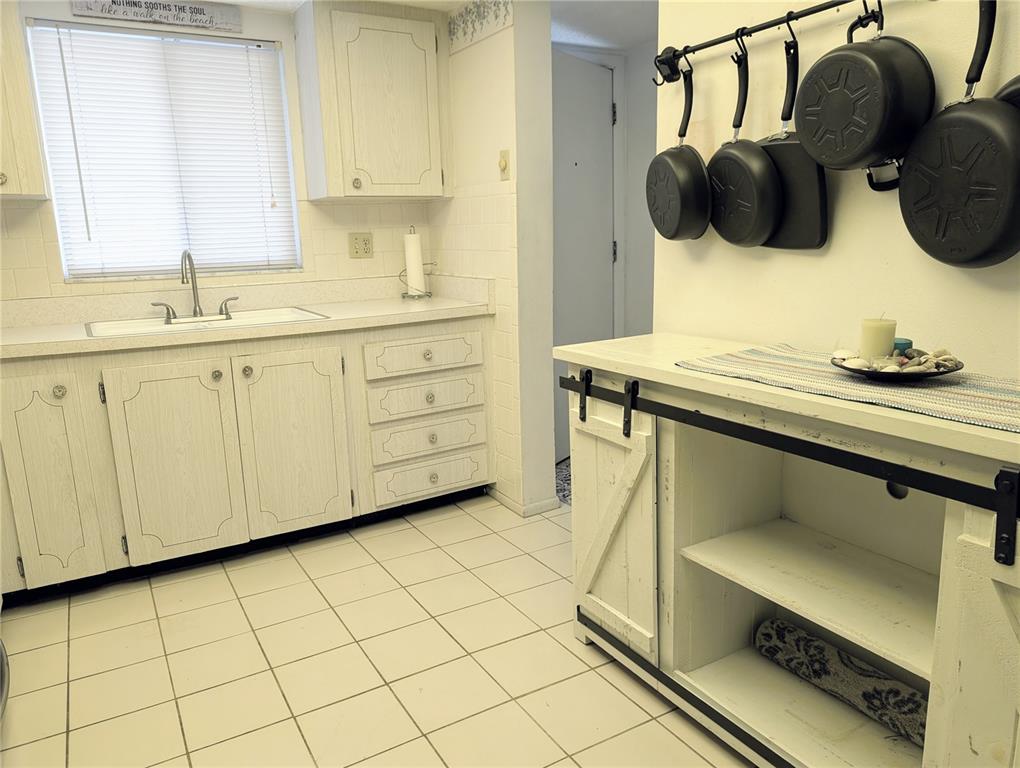 A kitchen features white cabinets, tiled flooring, a sink, and a wall-mounted pot rack — 3564 LAKE BAYSHORE DRIVE UNIT K-203, BRADENTON, FL