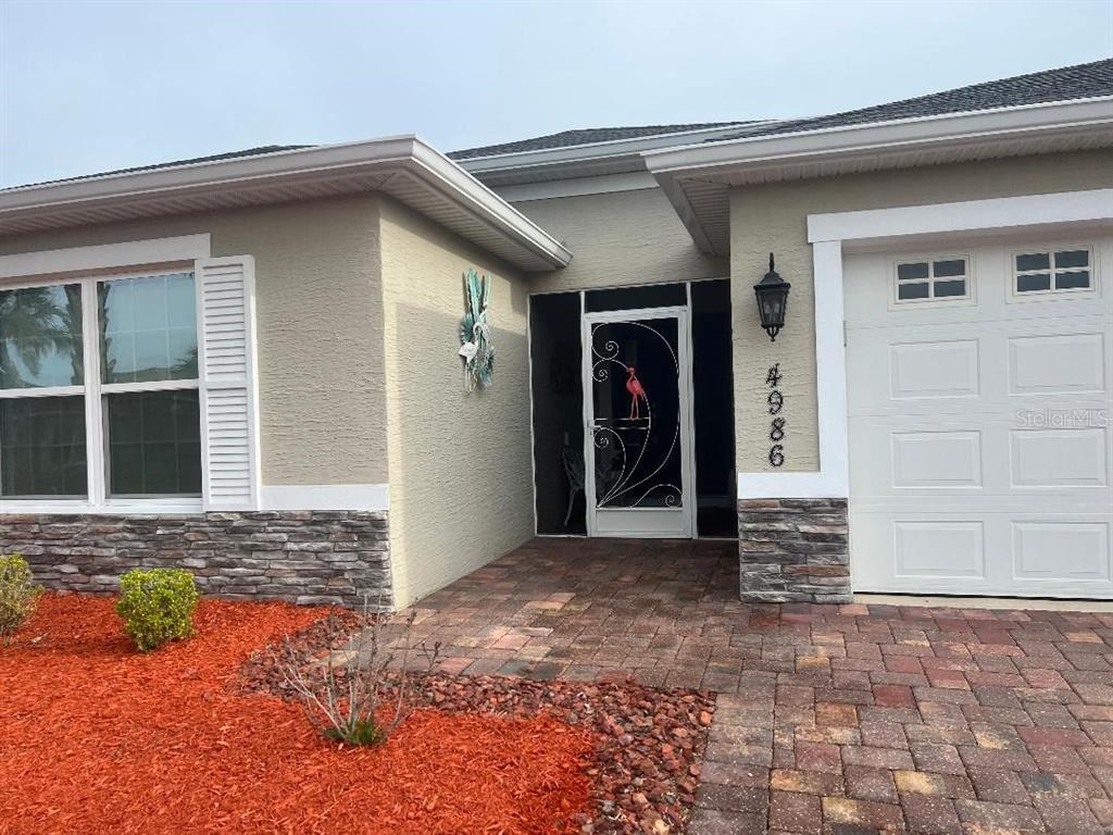 The exterior of a house features a stone-accented facade, a paved walkway, and a screen door — 4986 BELTED KINGFISHER DRIVE, OXFORD, FL