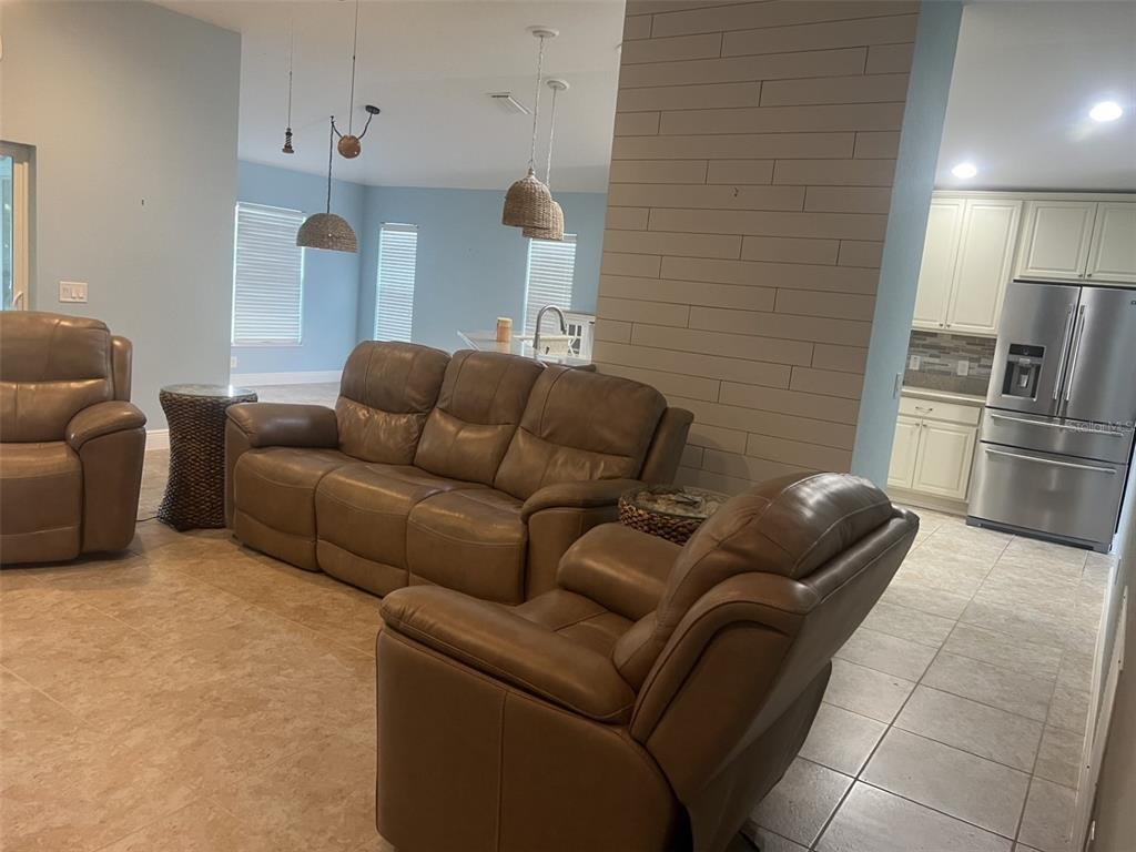 A living room with brown leather furniture, tile flooring, and a shiplap accent wall — 4986 BELTED KINGFISHER DRIVE, OXFORD, FL