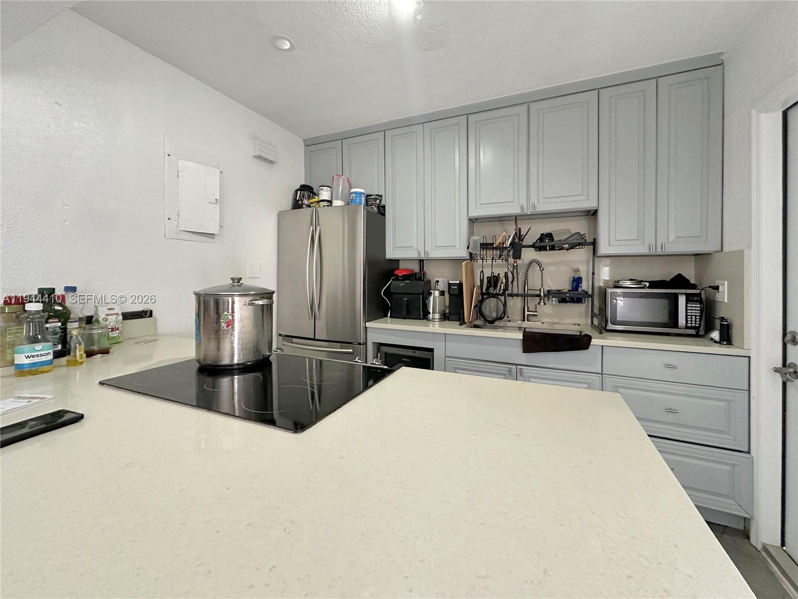 A kitchen features light gray cabinets, a stainless steel refrigerator, and a large island cooktop — 971 79th Ter, Miami Beach FL 33141, MIAMI BEACH, FL