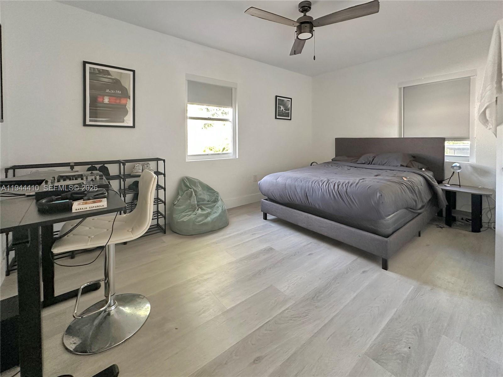 A bedroom features light wood-look flooring, a gray upholstered bed, a desk, and a ceiling fan — 971 79th Ter, Miami Beach FL 33141, MIAMI BEACH, FL