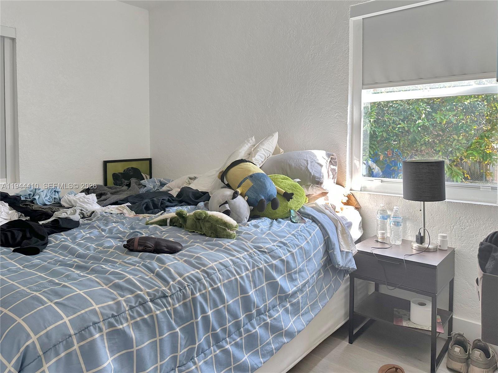 A bedroom features a blue plaid comforter, a nightstand with a lamp, and a window — 971 79th Ter, Miami Beach FL 33141, MIAMI BEACH, FL