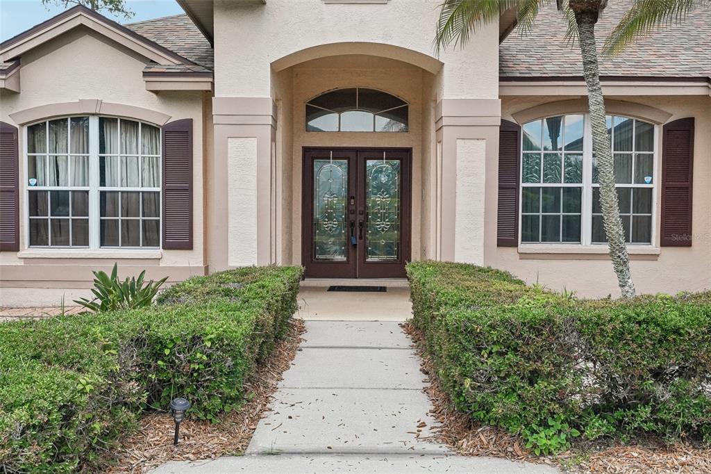 The front exterior of a house features a concrete walkway leading to double glass doors — 1008 ROBINWOOD DRIVE, OLDSMAR, FL