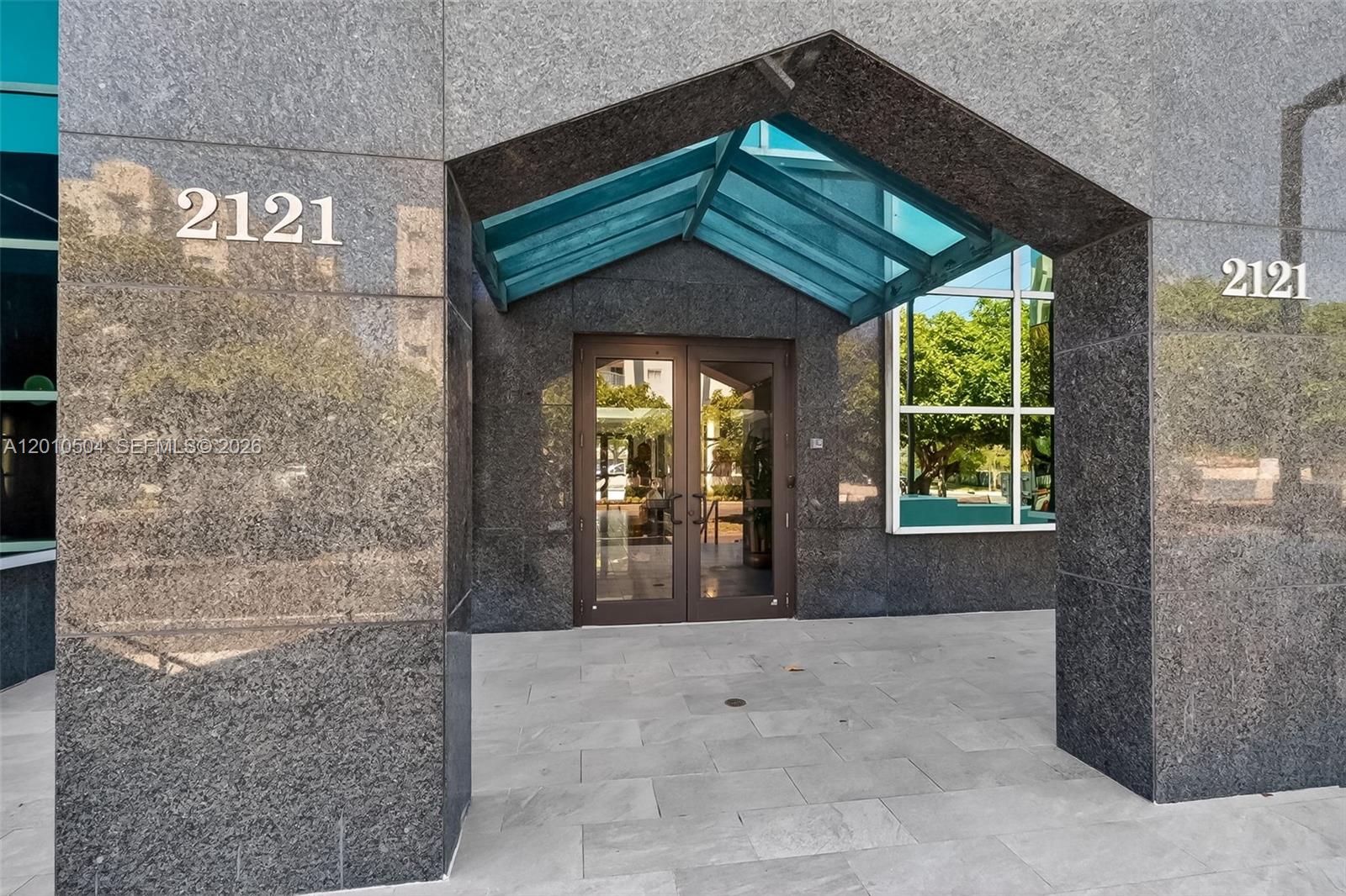 The exterior entrance of a building features dark granite walls, a glass awning, and double doors — 2121 SW 3rd Ave # 200, Miami FL 33129, MIAMI, FL