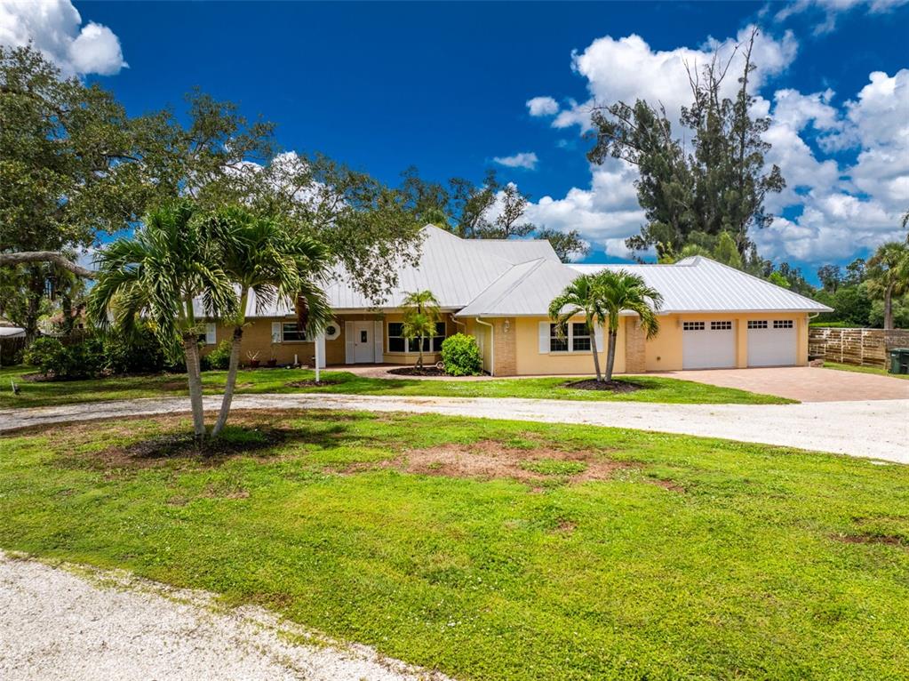 A single-story house with a white metal roof, yellow siding, and a gravel driveway — 200 S OXFORD DRIVE, ENGLEWOOD, FL