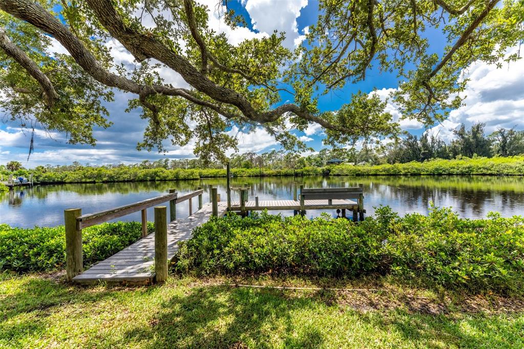 A wooden dock extends into a calm canal surrounded by lush green trees and vegetation — 200 S OXFORD DRIVE, ENGLEWOOD, FL