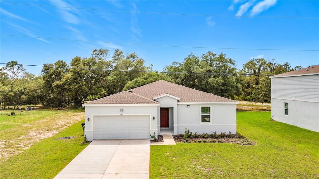 A single-story house with a light-colored exterior, a two-car garage, and a red front door — 1414 ORLANDO COURT, POINCIANA, FL
