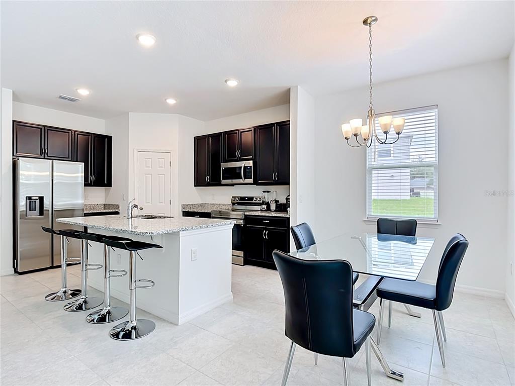 A kitchen with dark cabinets, granite countertops, and a dining area with a glass table — 1414 ORLANDO COURT, POINCIANA, FL