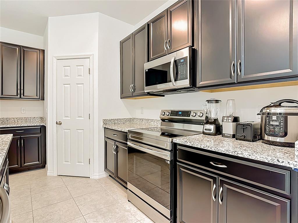 A kitchen features dark wood cabinets, granite countertops, stainless steel appliances, and tile flooring — 1414 ORLANDO COURT, POINCIANA, FL