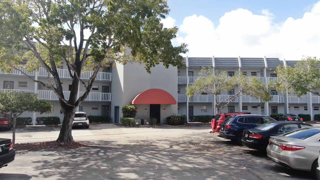 A three-story apartment building with a red awning entrance and a parking lot in front — 6570 Royal Palm Boulevard # 106j, Margate FL 33063, MARGATE, FL