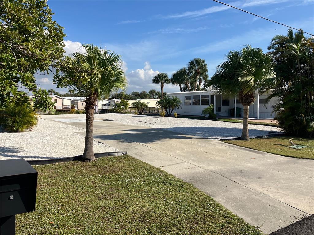 A concrete driveway leads to a white mobile home surrounded by palm trees and gravel — 1447 FLAMINGO DRIVE, ENGLEWOOD, FL
