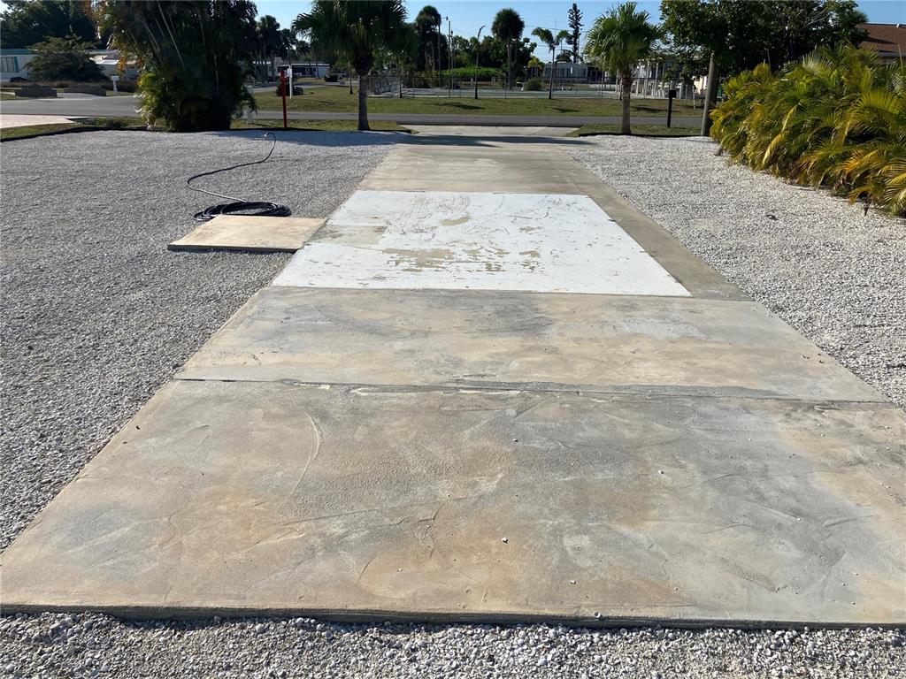 A concrete driveway pad sits between gravel areas in a residential outdoor space — 1447 FLAMINGO DRIVE, ENGLEWOOD, FL