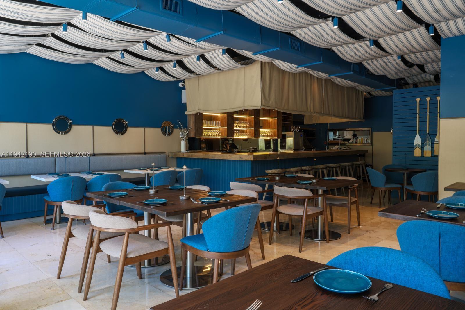 A restaurant interior features blue walls, wooden tables, blue upholstered chairs, and a draped ceiling — 1965 NE 2nd St, Deerfield Beach FL 33441, DEERFIELD BEACH, FL