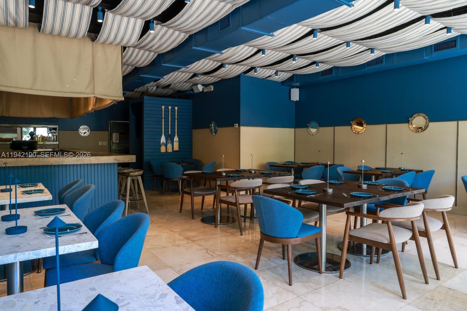 A restaurant dining room features blue walls, striped fabric ceiling drapes, and marble-topped tables — 1965 NE 2nd St, Deerfield Beach FL 33441, DEERFIELD BEACH, FL
