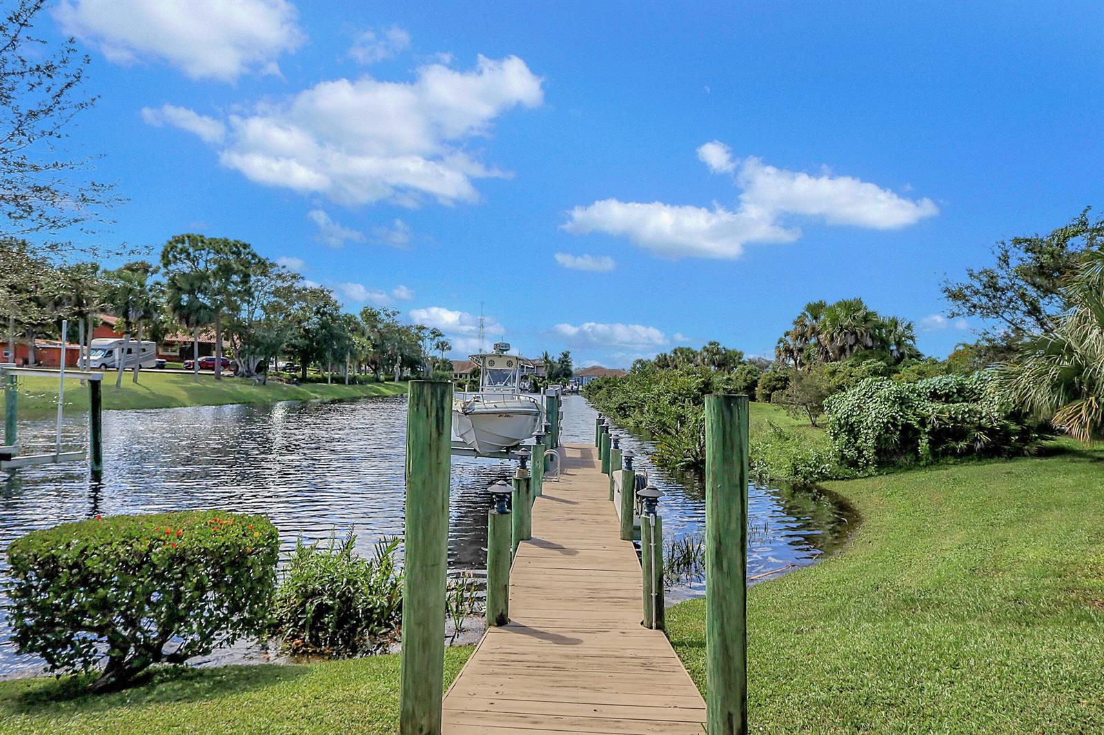 A wooden boat dock extends into a canal with a boat on a lift — 7186 SW Quiet River Court, Stuart FL 34997, STUART, FL