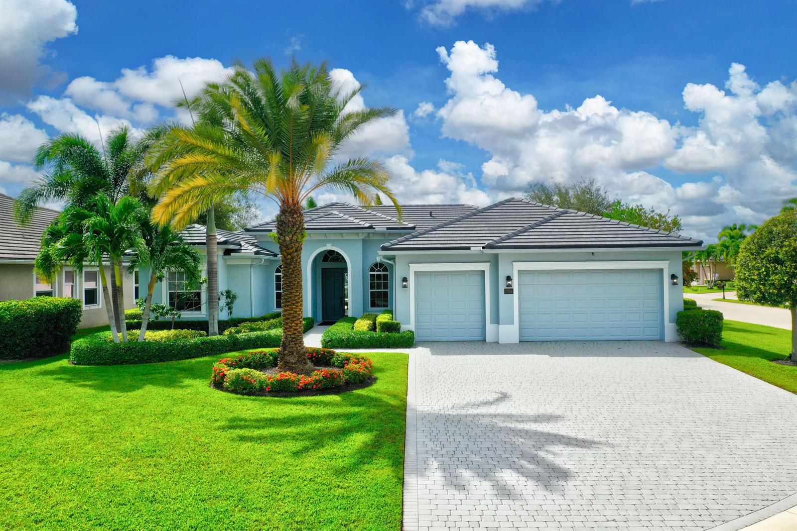 A light blue single-story house with a tile roof, three-car garage, and a palm tree — 7186 SW Quiet River Court, Stuart FL 34997, STUART, FL