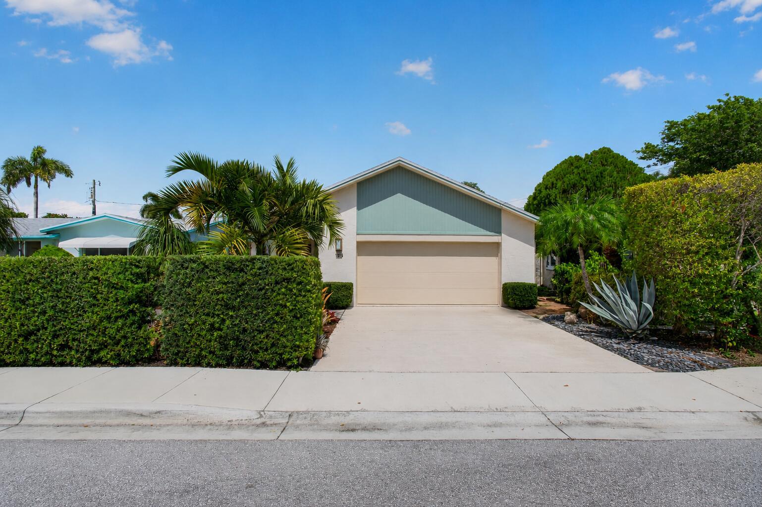 A single-story house with a beige garage door, light green gable, and manicured hedges — 1315 N Lakeside Drive, FL 33460, FL