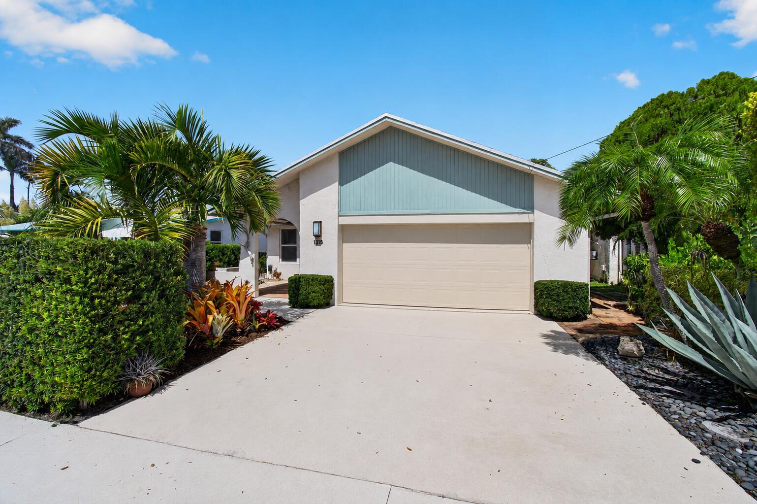 A single-story house with a beige garage door, light blue siding, and lush tropical landscaping — 1315 N Lakeside Drive, FL 33460, FL