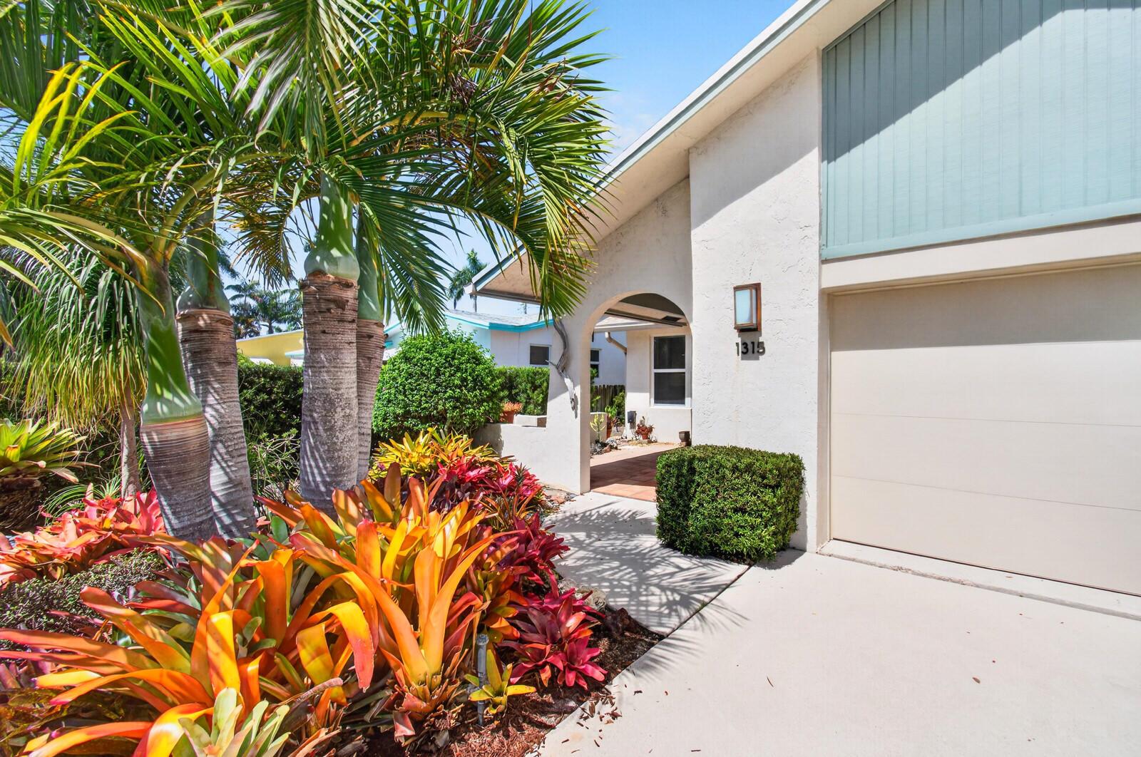 A house exterior features a beige garage, a palm tree, and colorful bromeliad landscaping — 1315 N Lakeside Drive, FL 33460, FL