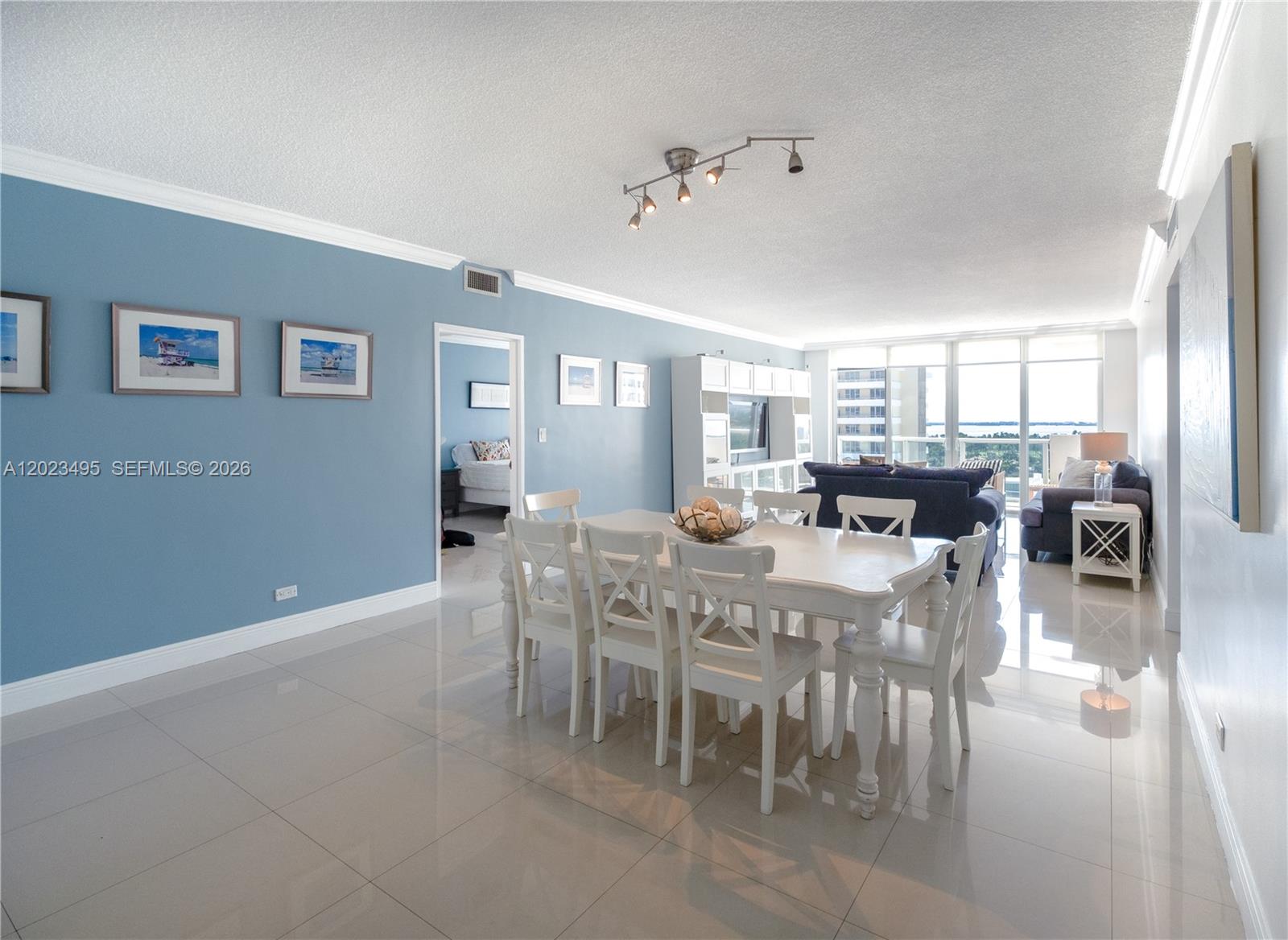 A dining area with a white table and chairs sits before a living room — 5601 Collins Ave # 1420, Miami Beach FL 33140, MIAMI BEACH, FL