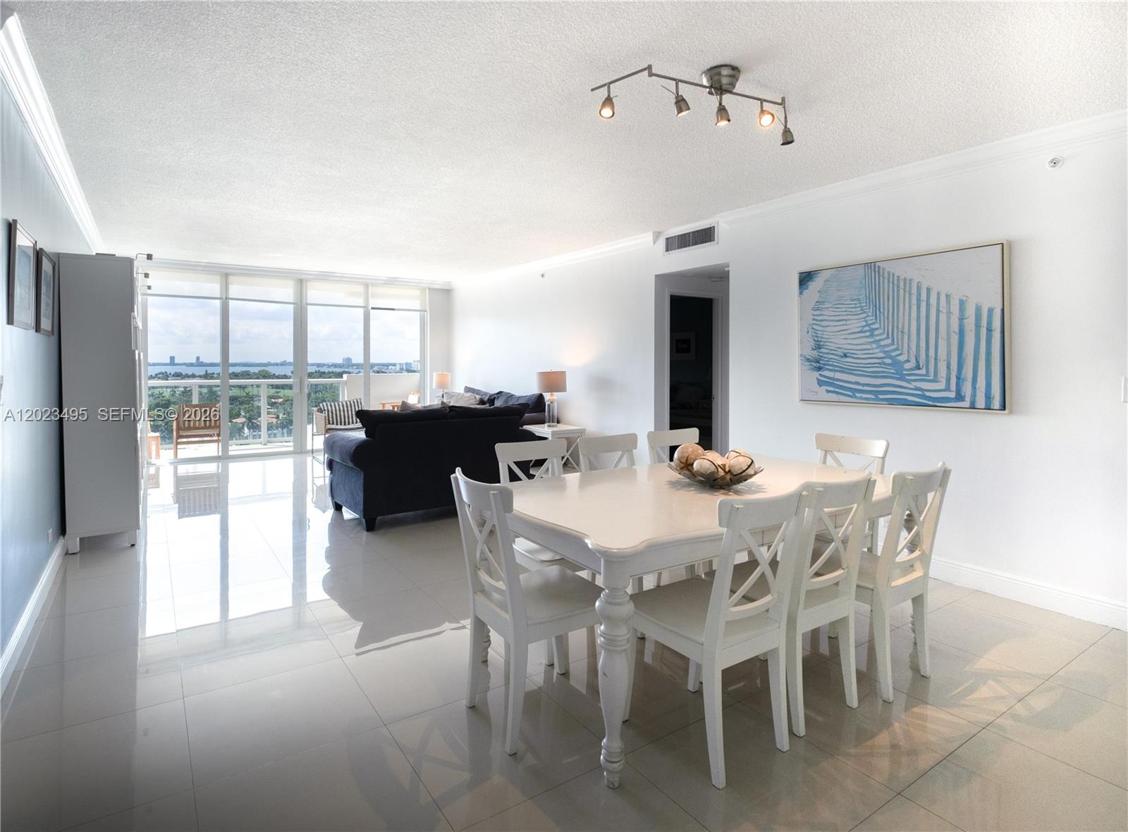 A dining area with a white table and chairs sits before a bright living room — 5601 Collins Ave # 1420, Miami Beach FL 33140, MIAMI BEACH, FL