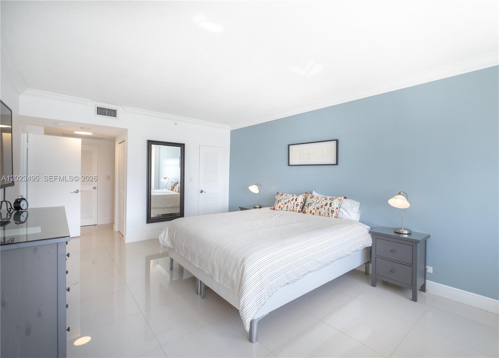 A bedroom features a bed with striped bedding, gray nightstands, and a blue accent wall — 5601 Collins Ave # 1420, Miami Beach FL 33140, MIAMI BEACH, FL