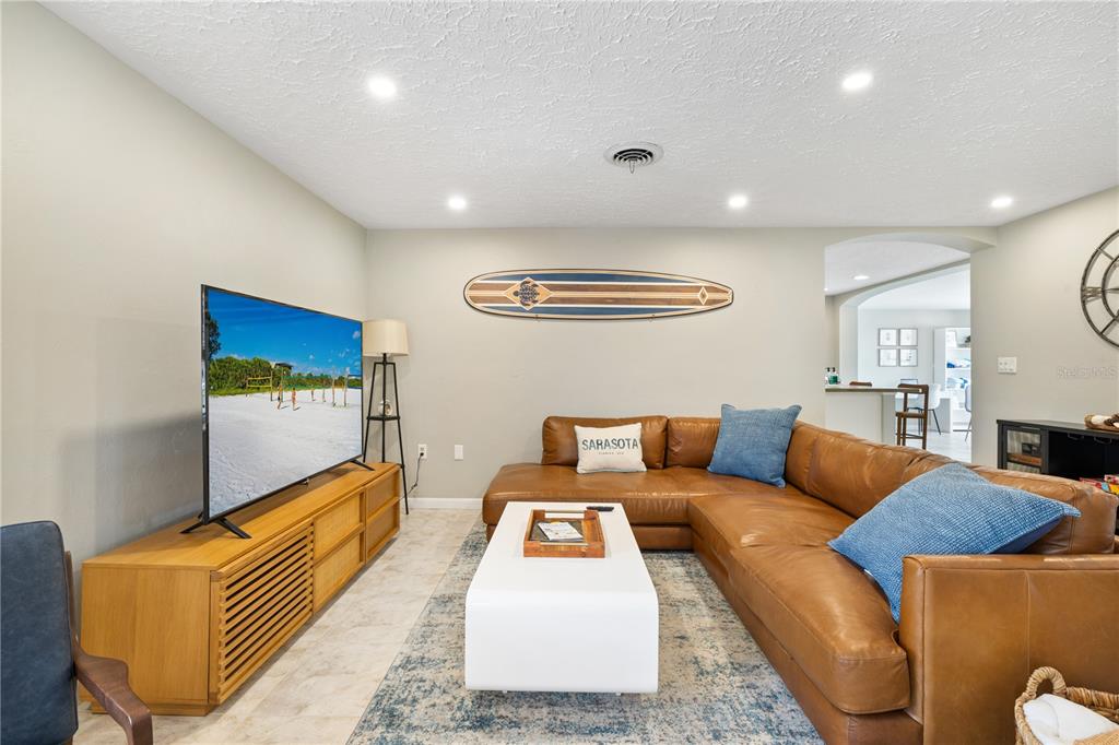 A living room features a brown leather sectional, a white coffee table, and a surfboard decoration — 2365 BAY STREET, SARASOTA, FL