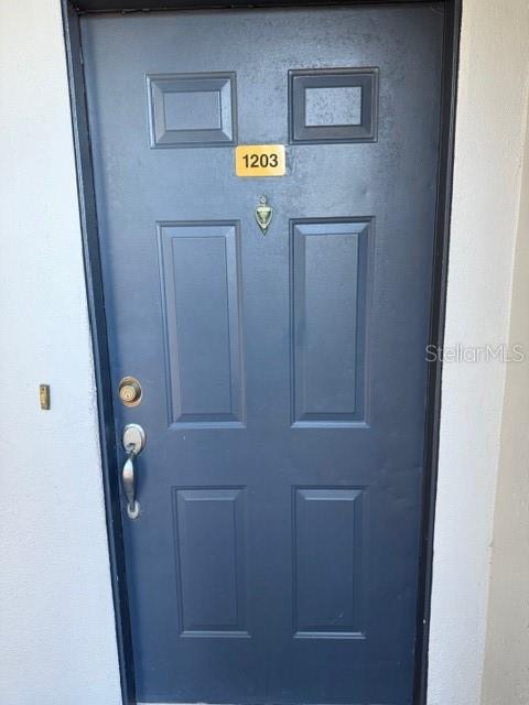 A dark blue, six-panel exterior door features a gold number plate reading 1203 — 1203 CLUBSIDE DRIVE UNIT 1203, LONGWOOD, FL