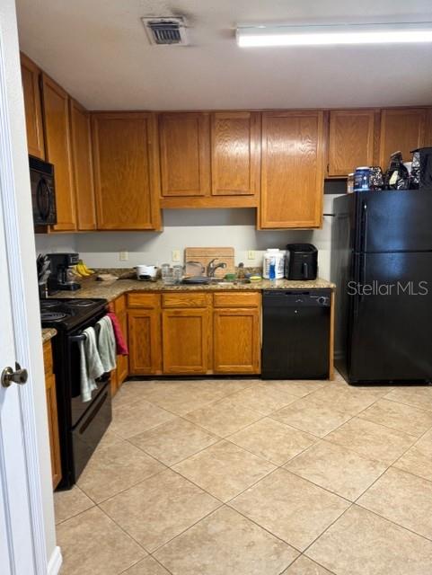 A kitchen features oak cabinets, black appliances, and light-colored tile flooring — 1203 CLUBSIDE DRIVE UNIT 1203, LONGWOOD, FL