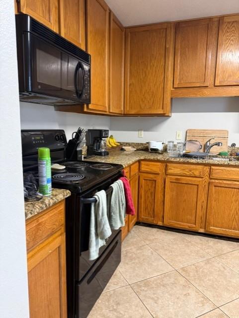 A kitchen features oak cabinets, a black microwave, a black stove, and tiled flooring — 1203 CLUBSIDE DRIVE UNIT 1203, LONGWOOD, FL