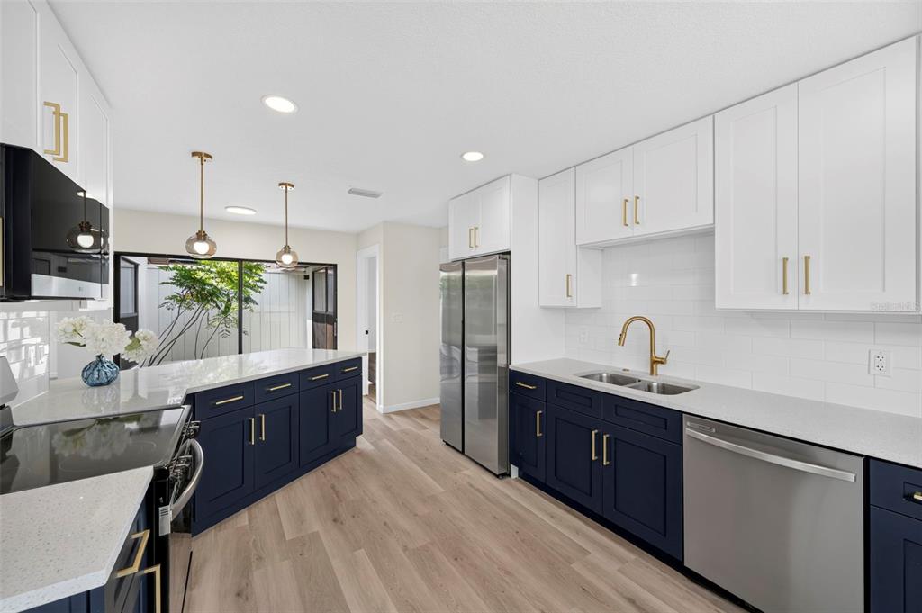 A kitchen features white upper cabinets, dark blue lower cabinets, stainless steel appliances, and wood flooring — 647 BONNIE BOULEVARD, PALM HARBOR, FL