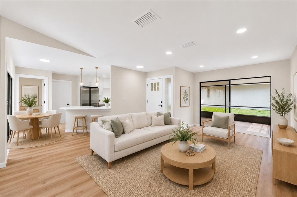 A bright, open-concept living and dining area features light wood flooring and neutral furniture — 647 BONNIE BOULEVARD, PALM HARBOR, FL